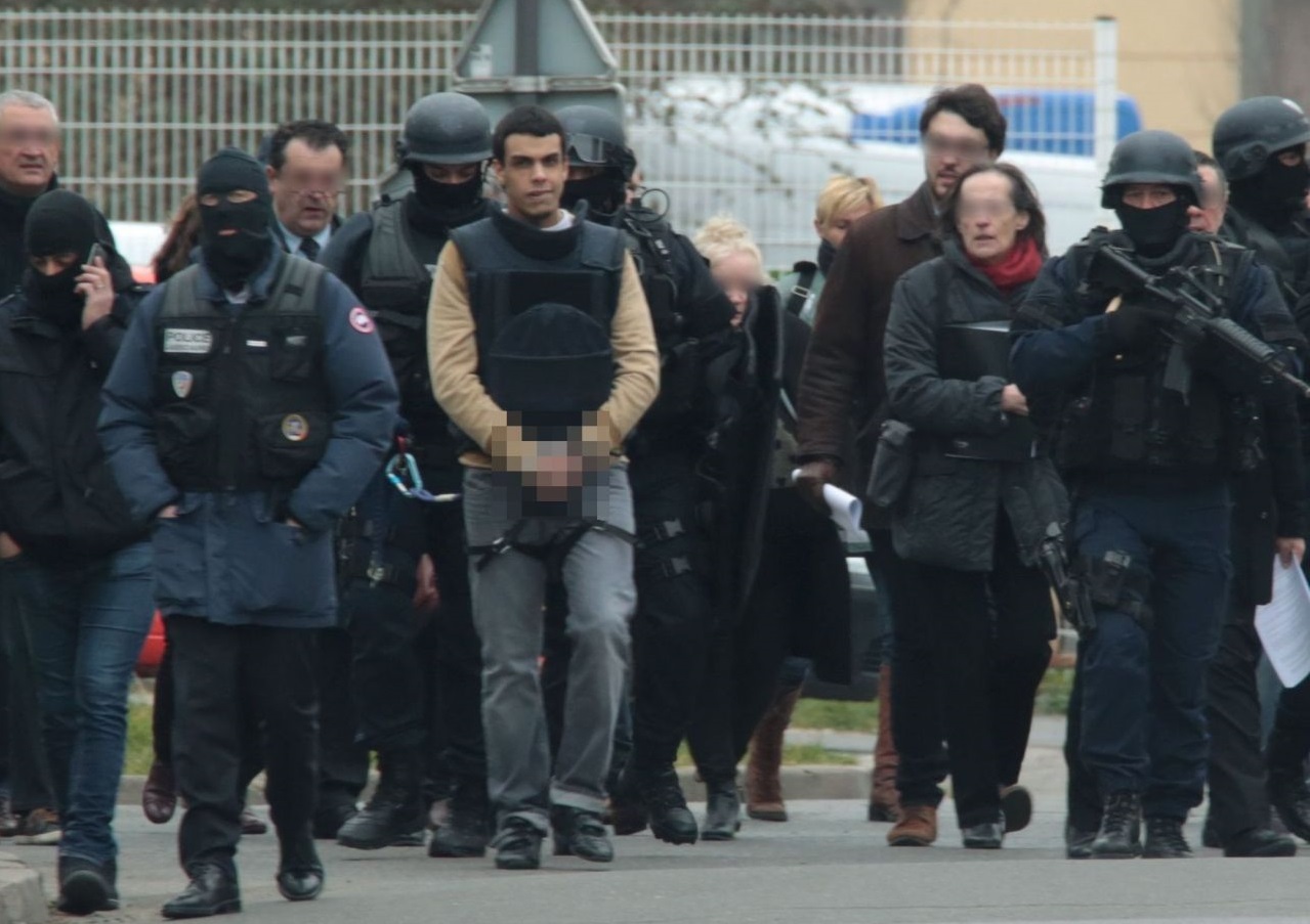 Sid Ahmed Ghlam menotté et encadré par les forces de police lors d'une reconstitution. D. R.